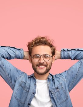 Vertical shot of relaxed carefree man keeps hands behind head, has positive expression, smiles pleasantly, listens something with interest, dressed in fashionable shirt, isolated over pink studio wall Vertical shot of relaxed carefree man keeps hands behind head, has positive expression, smiles pleasantly, listens something with interest, dressed in fashionable shirt, isolated over pink studio wall